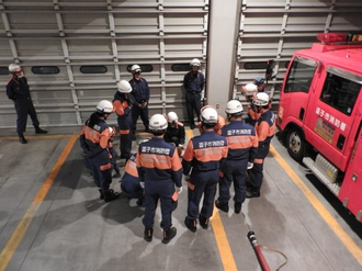 写真：消防隊員から指導を受ける団員たちの後ろ姿