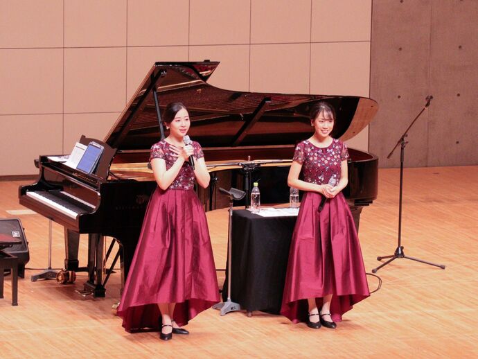 なぎさホールの舞台に山田姉妹が立っている。左側に立つ山田華さんが話している様子。